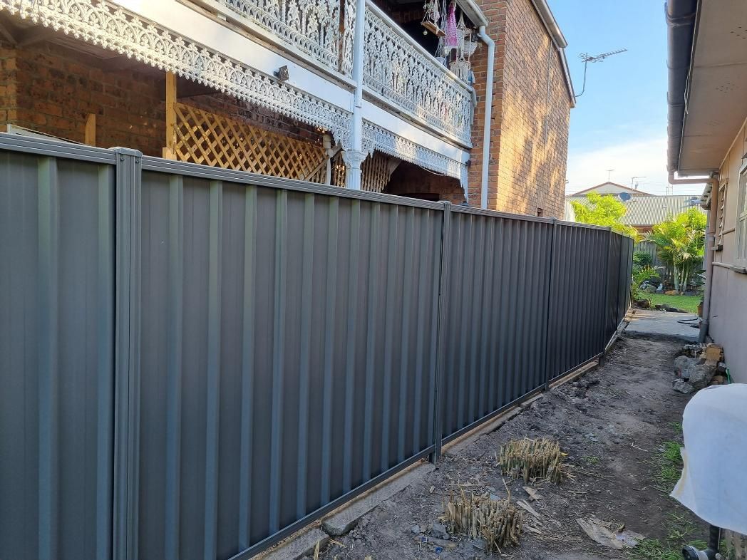 A Black Fence Is Sitting Next to A Brick Building — Quality Fencing Solutions in Ballina, NSW