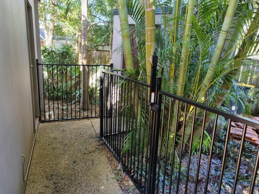 A Black Metal Fence Is Surrounded by Trees and Bushes — Quality Fencing Solutions in Ballina, NSW