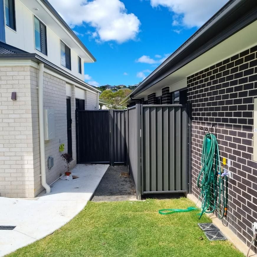 A Brick House with A Black Fence and A Green Hose — Quality Fencing Solutions in Ballina, NSW