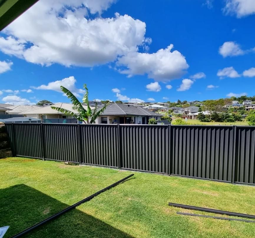 A Black Fence Surrounds a Lush Green Yard with Houses in The Background — Quality Fencing Solutions in Ballina, NSW