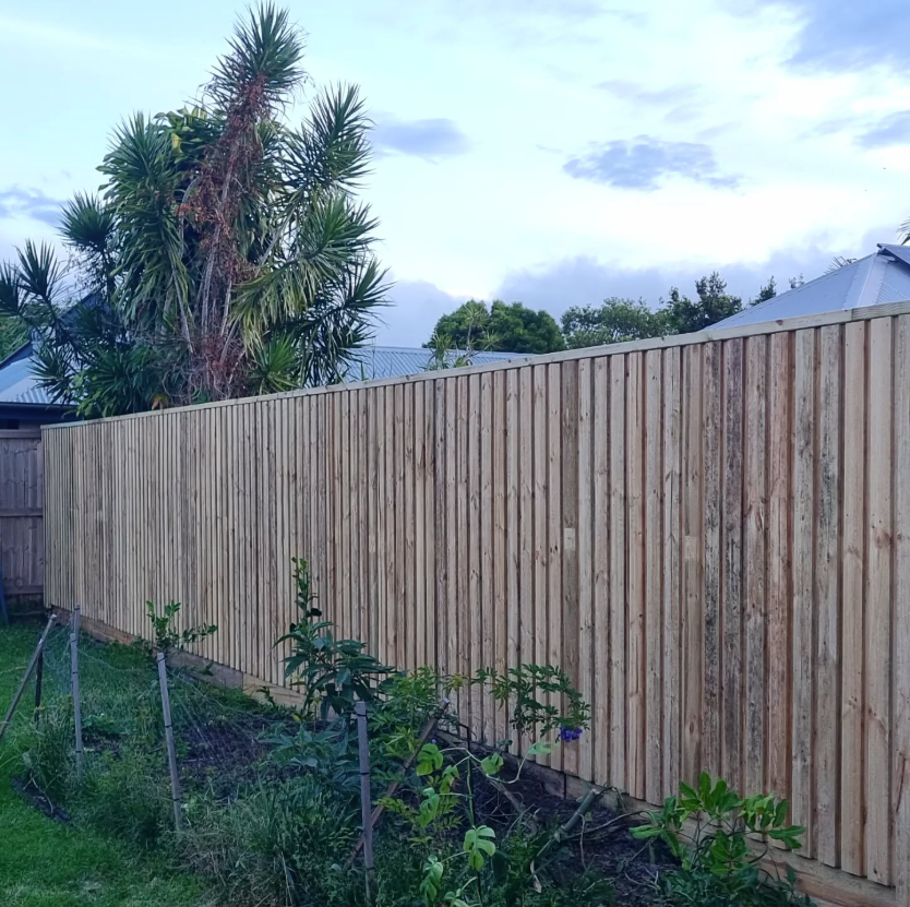 A White Fence Is Surrounded by Trees in A Backyard — Quality Fencing Solutions in Ballina, NSW