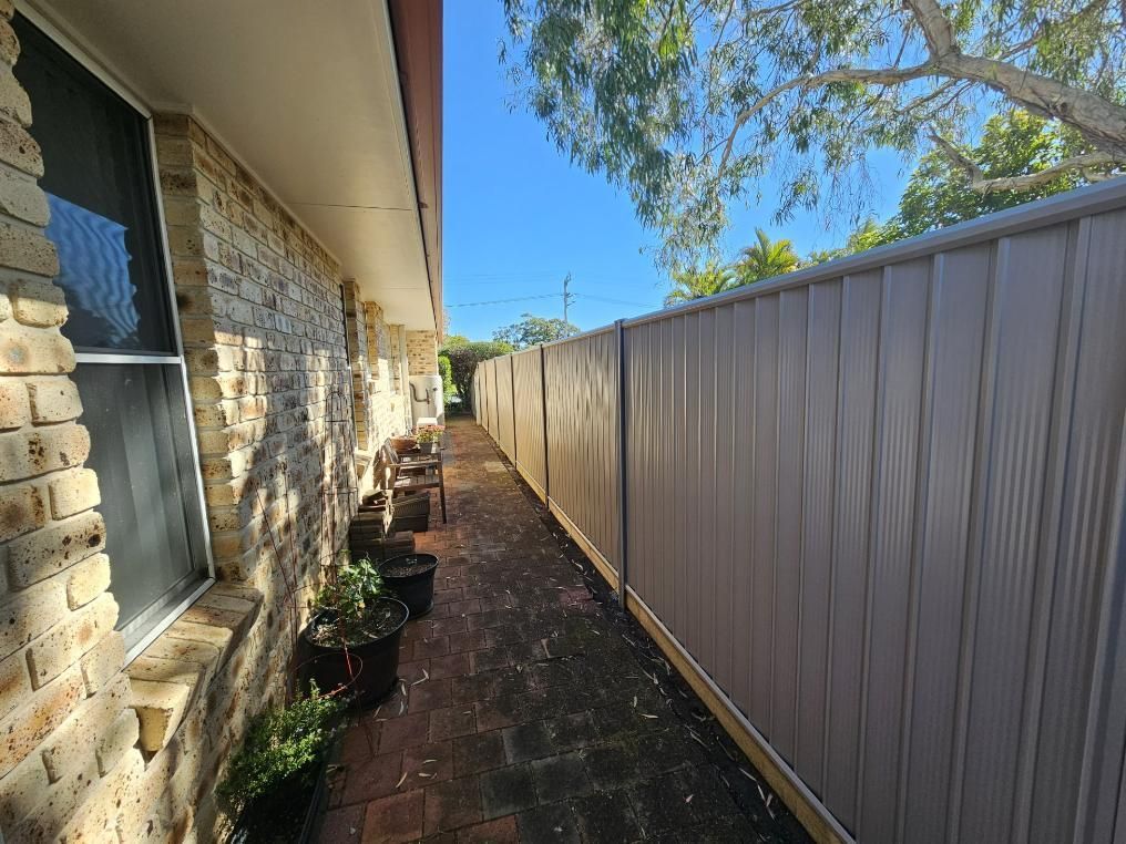 A Brick Building with A Fence Along the Side of It — Quality Fencing Solutions in Ballina, NSW