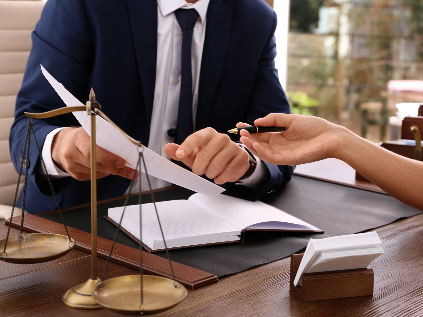 Avvocato che tiene in mano un documento, una bilancia della giustizia, mentre porge una penna a una persona per firmare i documenti.