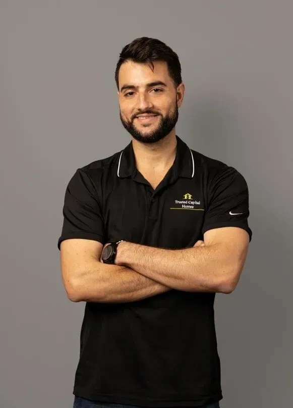 A man with a beard is wearing a black polo shirt and standing with his arms crossed.