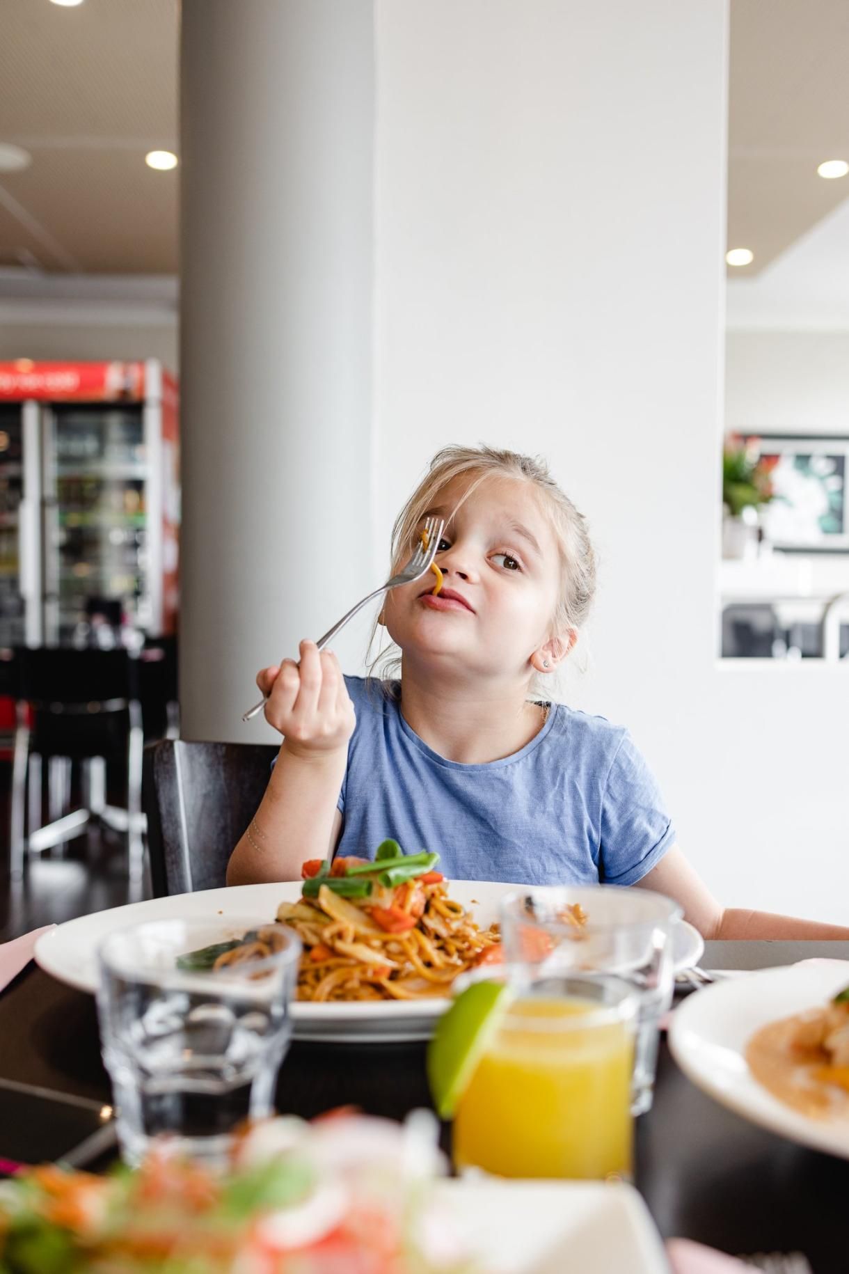 A Little Girl Is Sitting At A Table Eating Food With A Fork — Mod Thai Nelson Bay In Nelson Bay, NSW