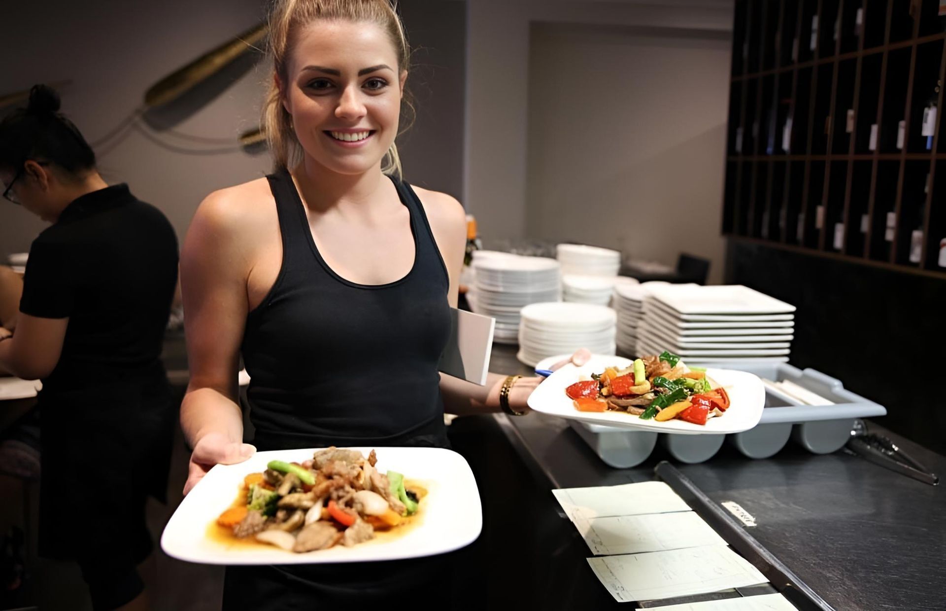 A Woman In A Black Tank Top Is Holding Two Plates Of Food — Mod Thai Nelson Bay In Nelson Bay, NSW