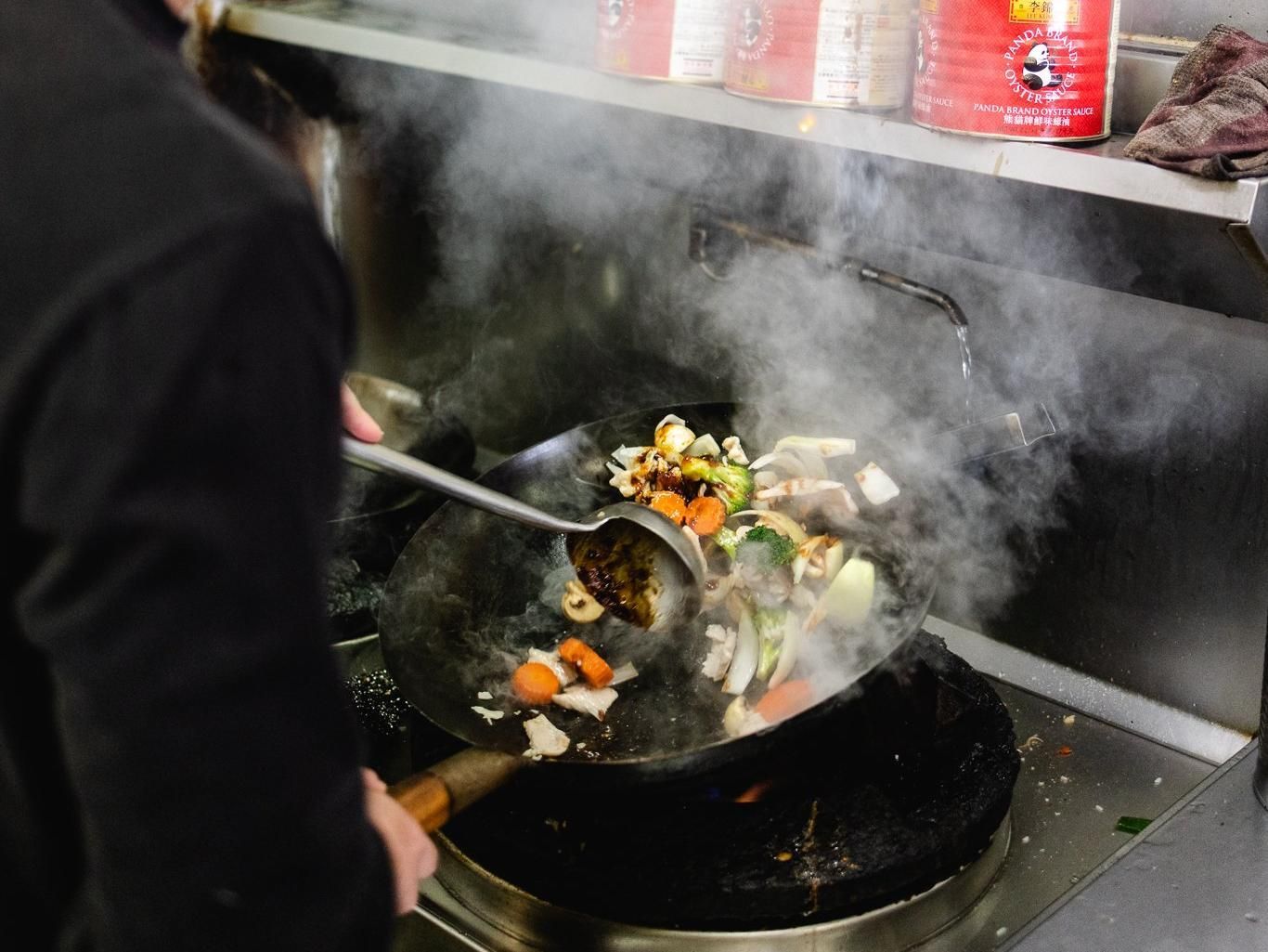 A Person Is Cooking Vegetables In A Wok On A Stove — Mod Thai Nelson Bay In Nelson Bay, NSW