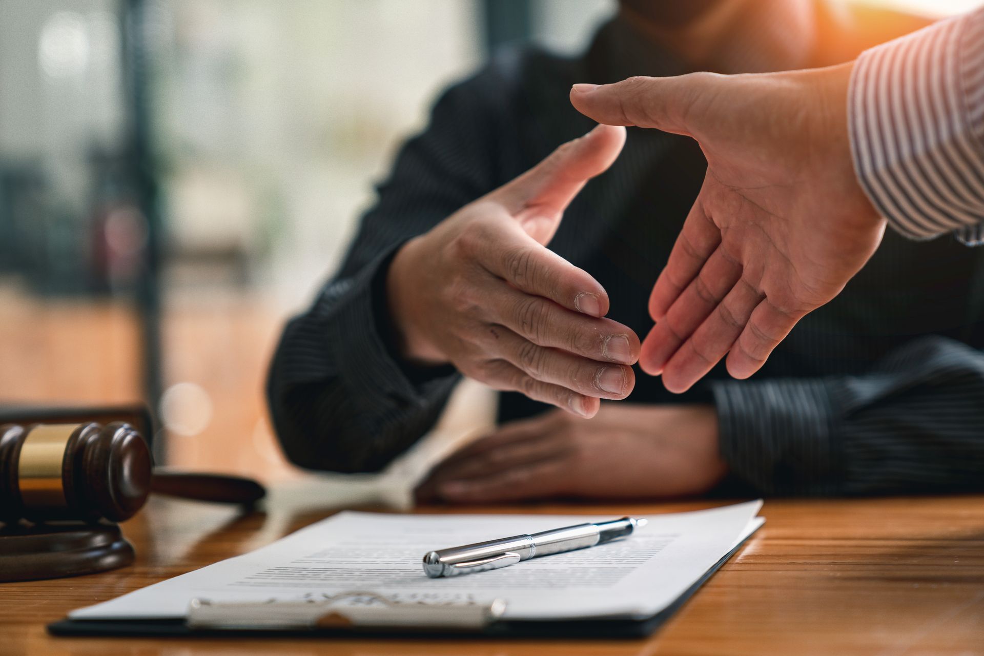Close-up of a solicitor, seated next to a wooden gavel, shaking hands with a client in their office. Close-up of a solicitor, seated next to a wooden gavel, shaking hands with a client in their office.