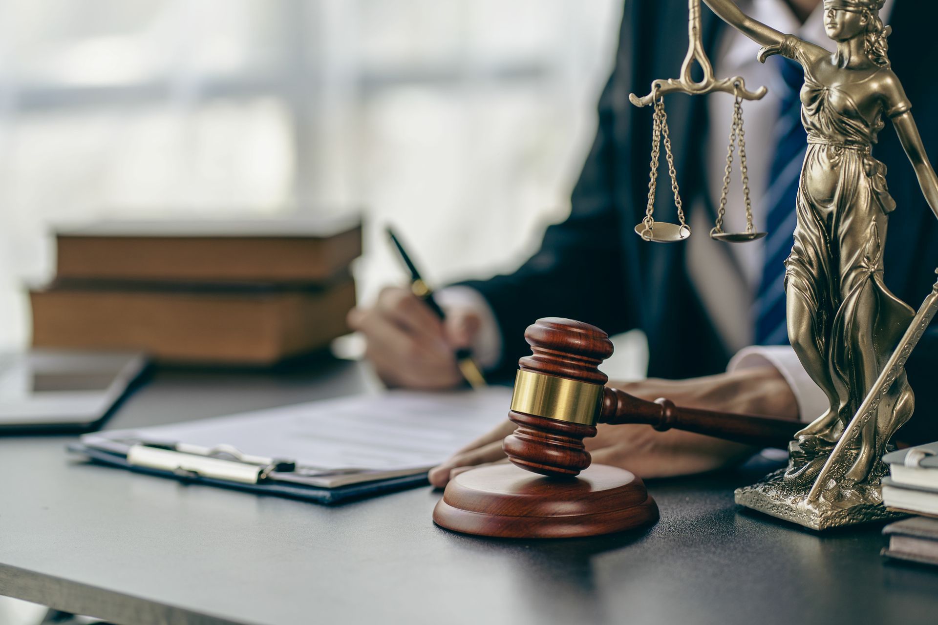 A criminal law solicitor working at their desk, next to a wooden gavel and a justice scale. A criminal law solicitor working at their desk, next to a wooden gavel and a justice scale.