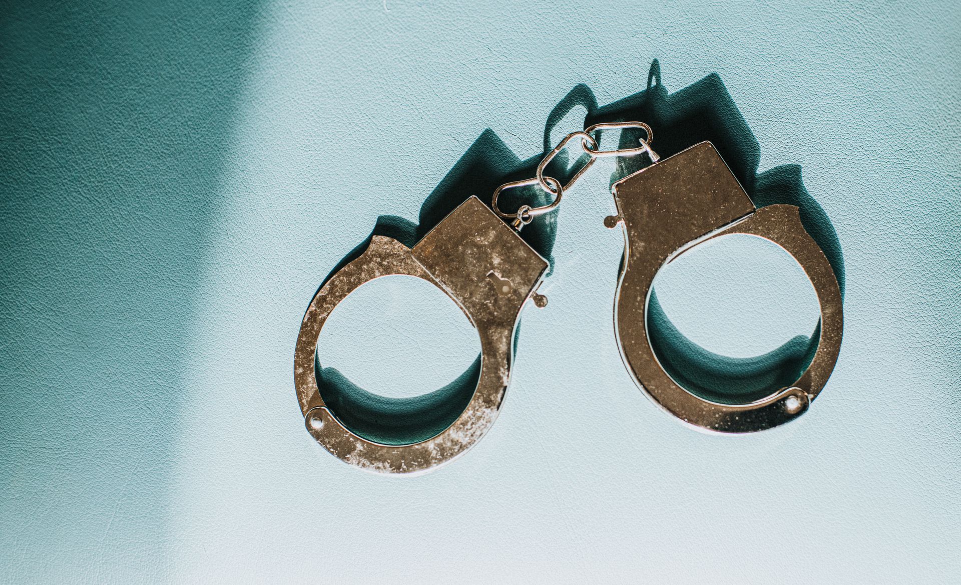 Close-up of handcuffs on a light blue surface.
