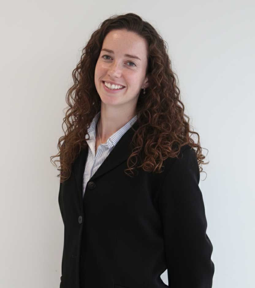 Woman with curly brown hair smiling in a black blazer and white collared shirt.