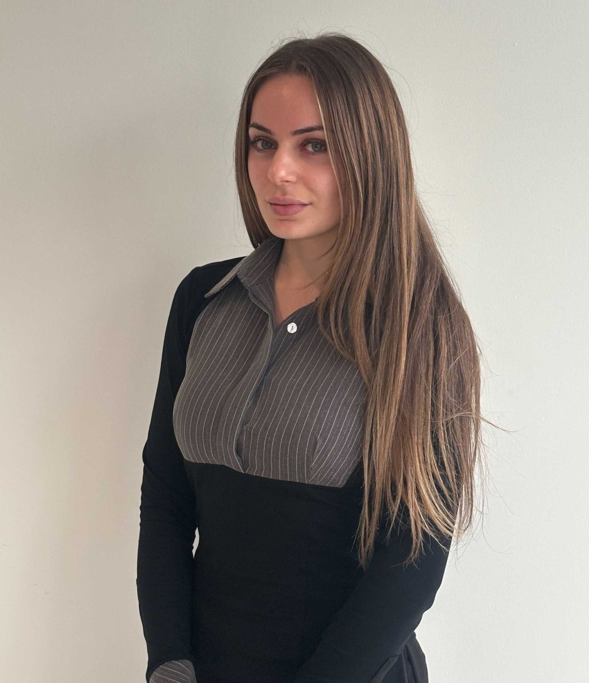 Woman with long, crimped brown hair, wearing a black top with gray patterned panel.