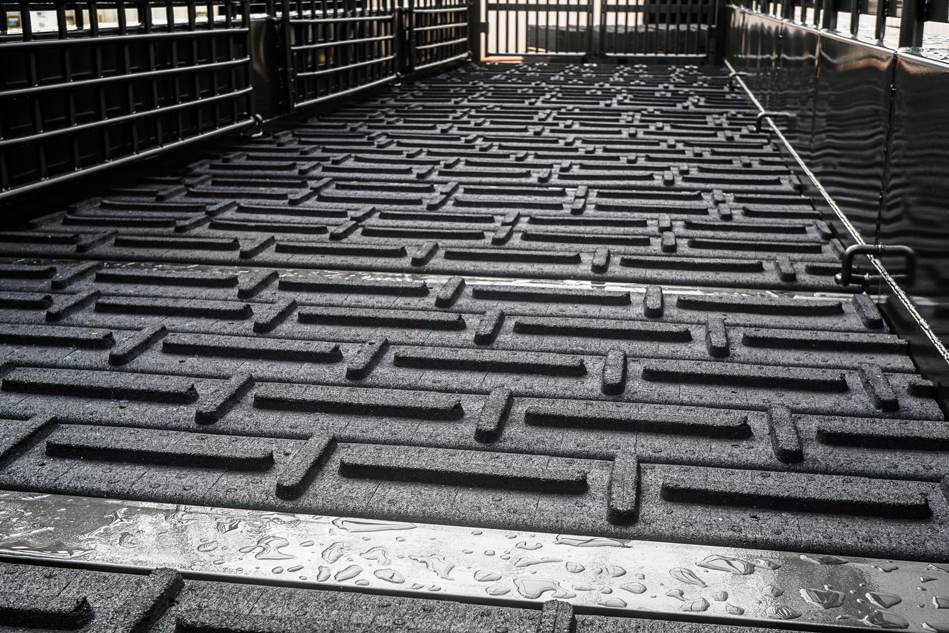 Black, patterned matting in a livestock chute, possibly for animal safety and traction.