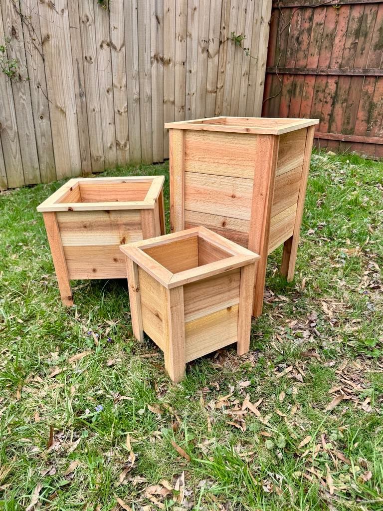 Three wooden planters are sitting on top of a lush green field.