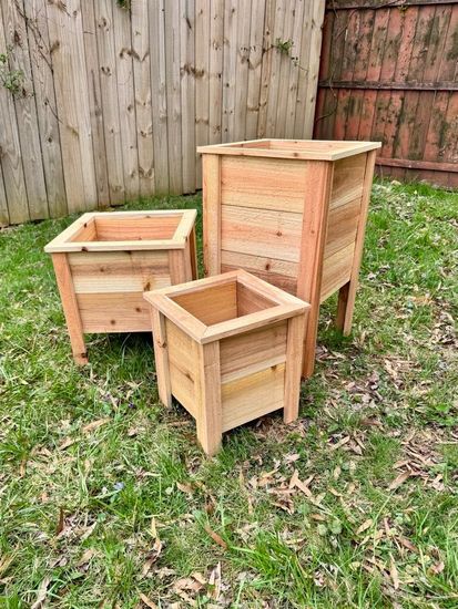 Three wooden planters are sitting on top of a lush green field.