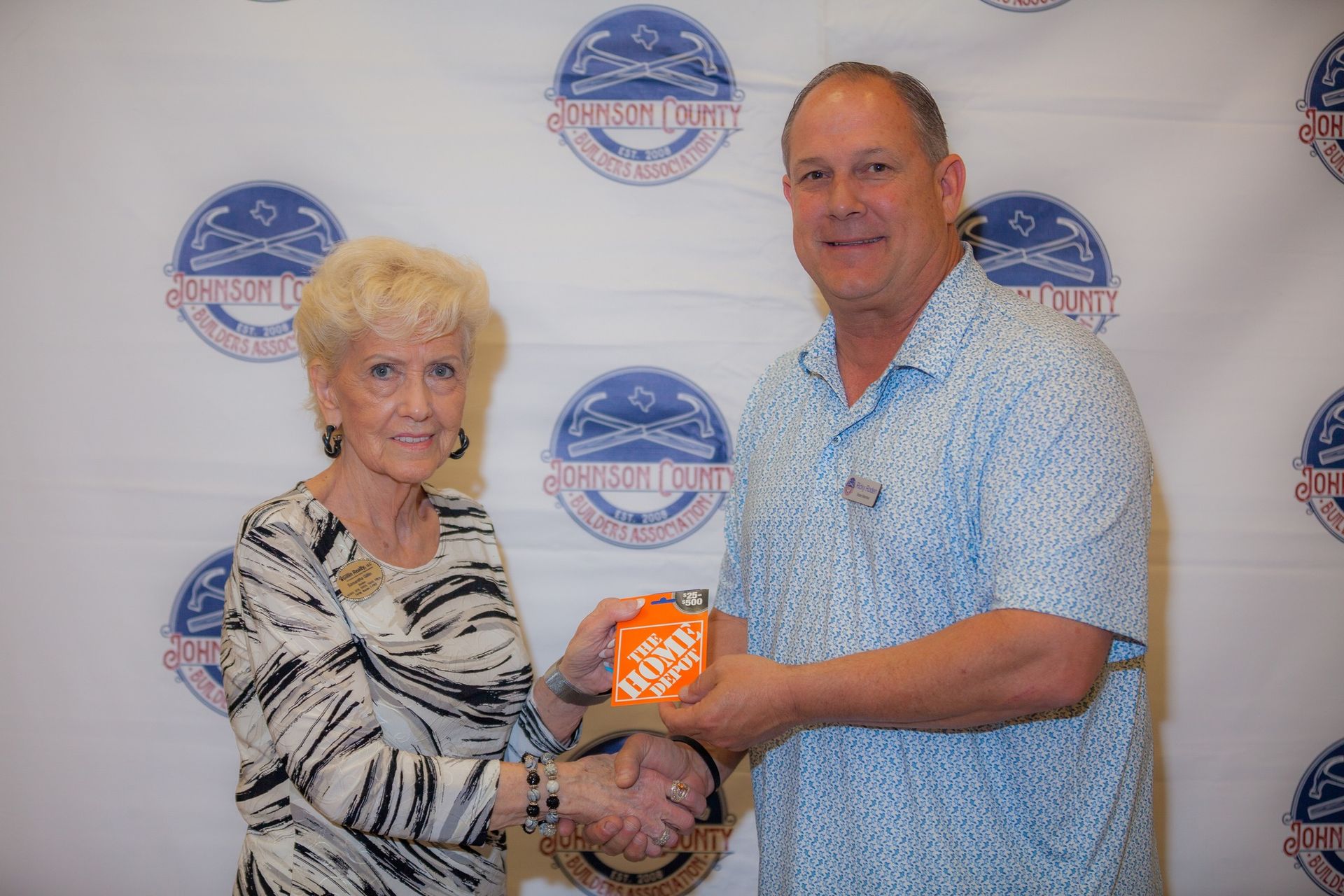 A man and a woman are shaking hands in front of a home depot sign.