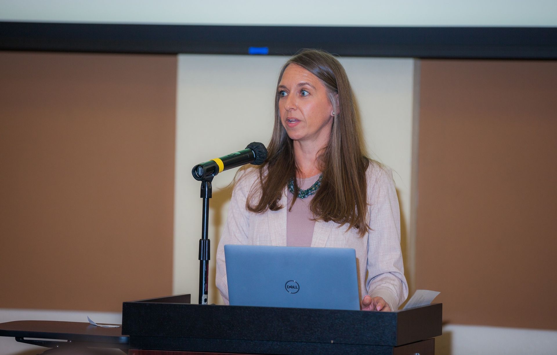 A woman is standing at a podium with a laptop and a microphone.