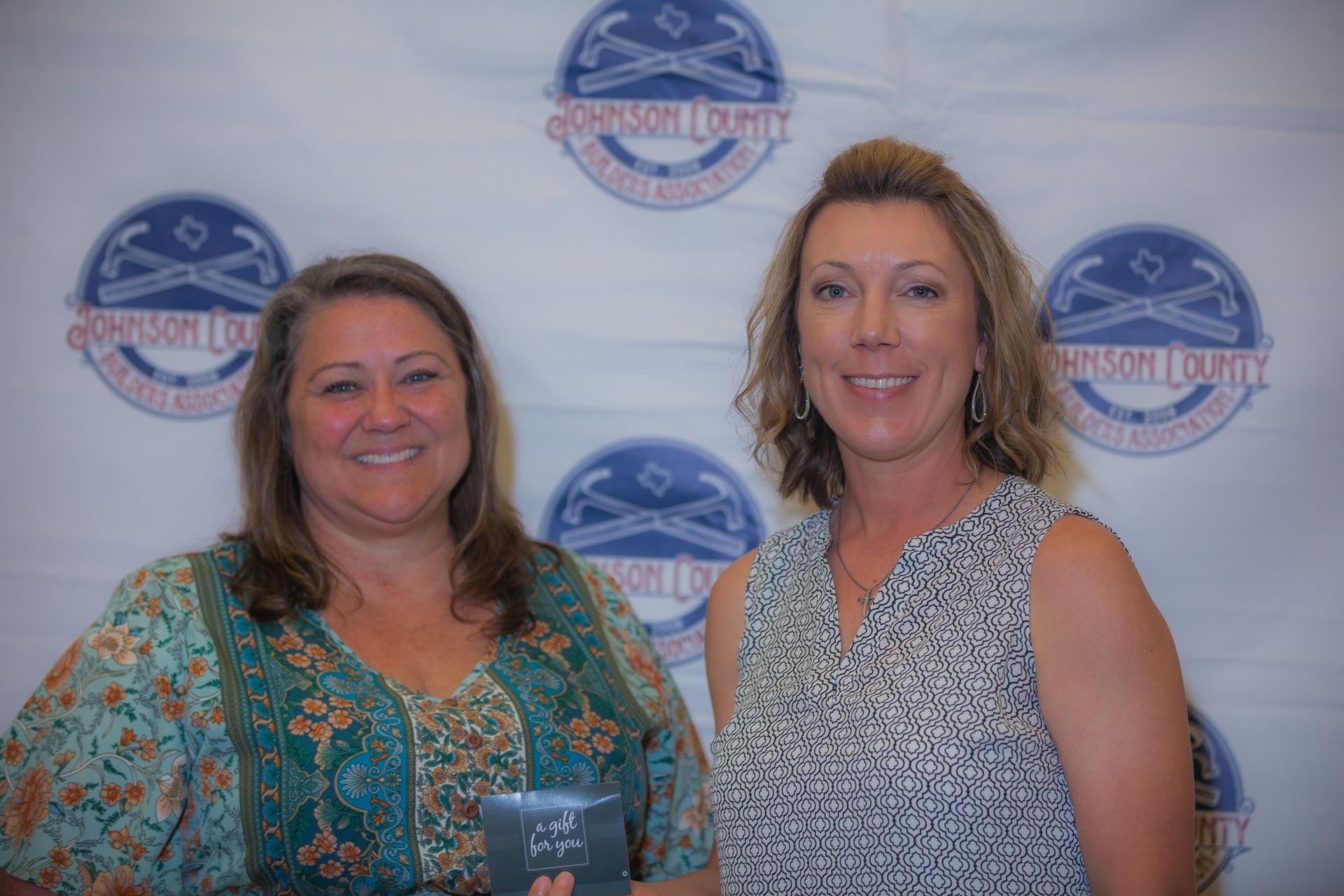 Two women are standing next to each other in front of a banner.