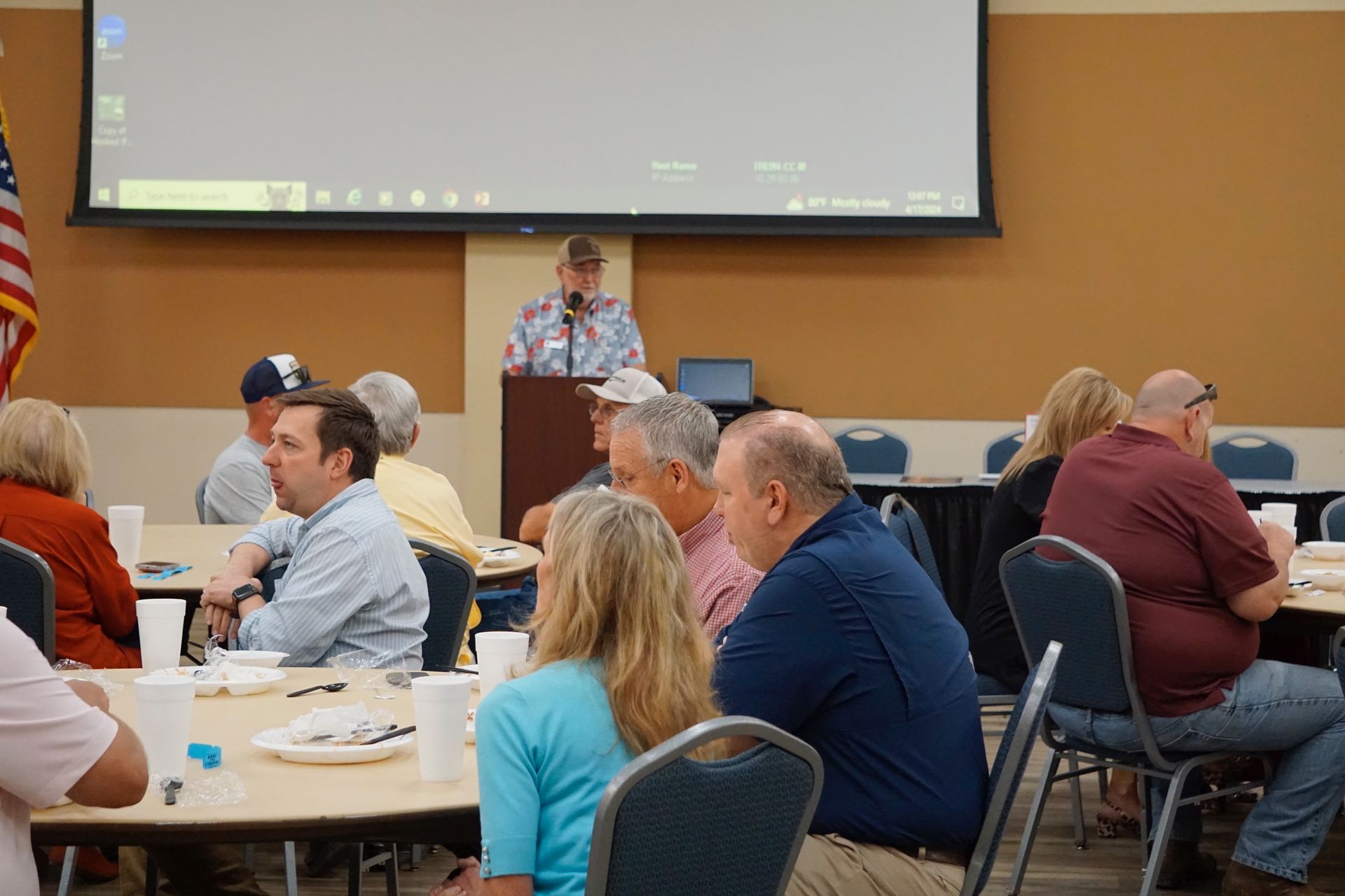 A group of people are sitting at tables in front of a projector screen.