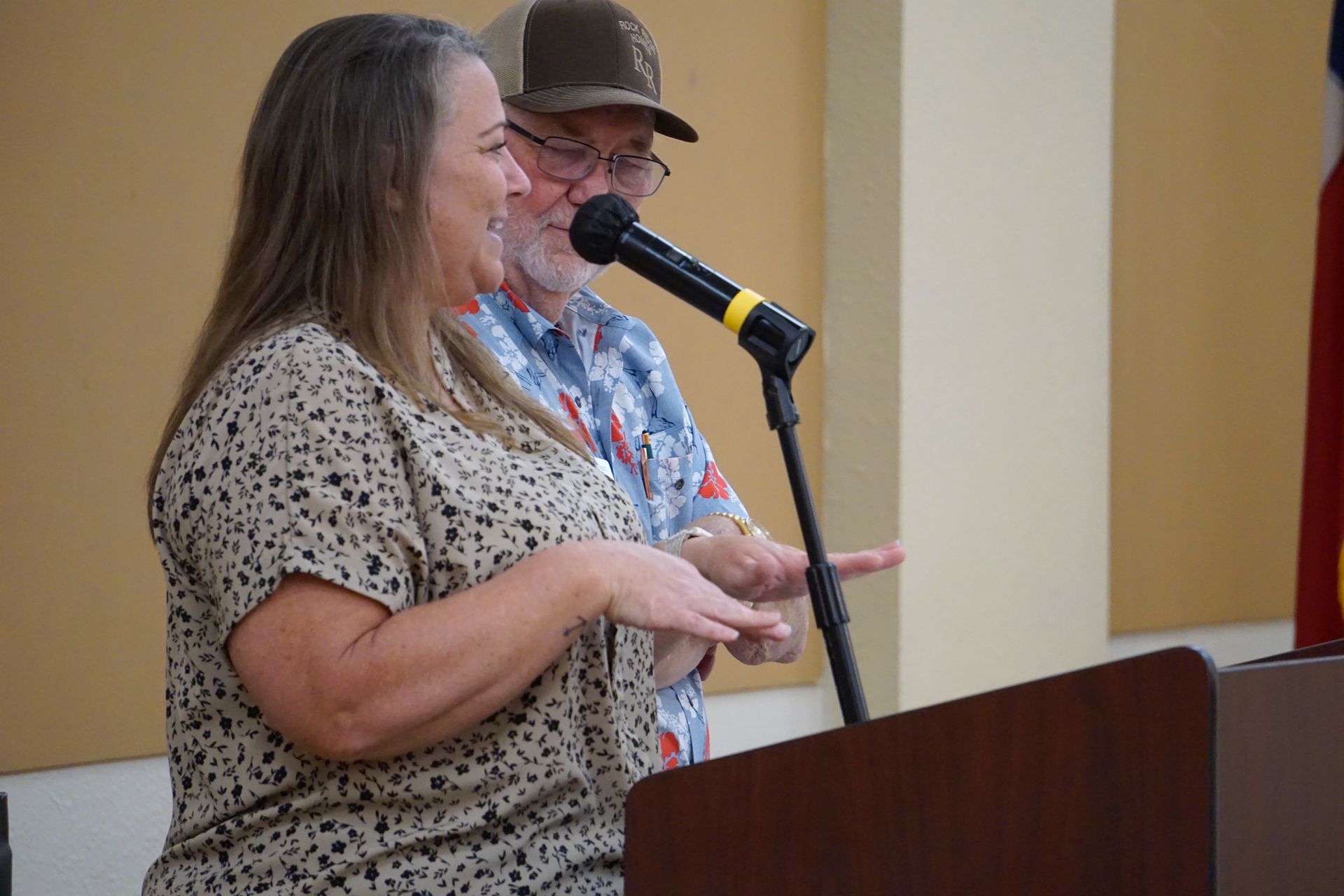 A man and a woman are standing at a podium talking into microphones.