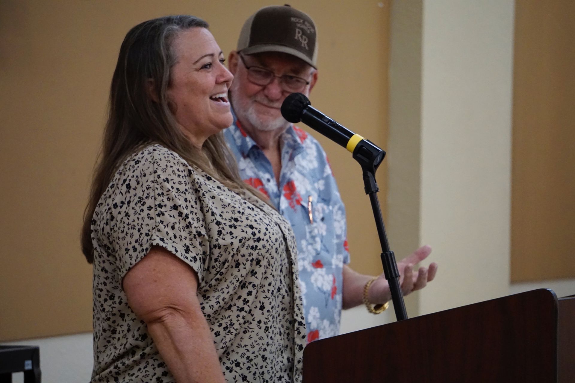 A man and a woman are standing at a podium talking into a microphone.