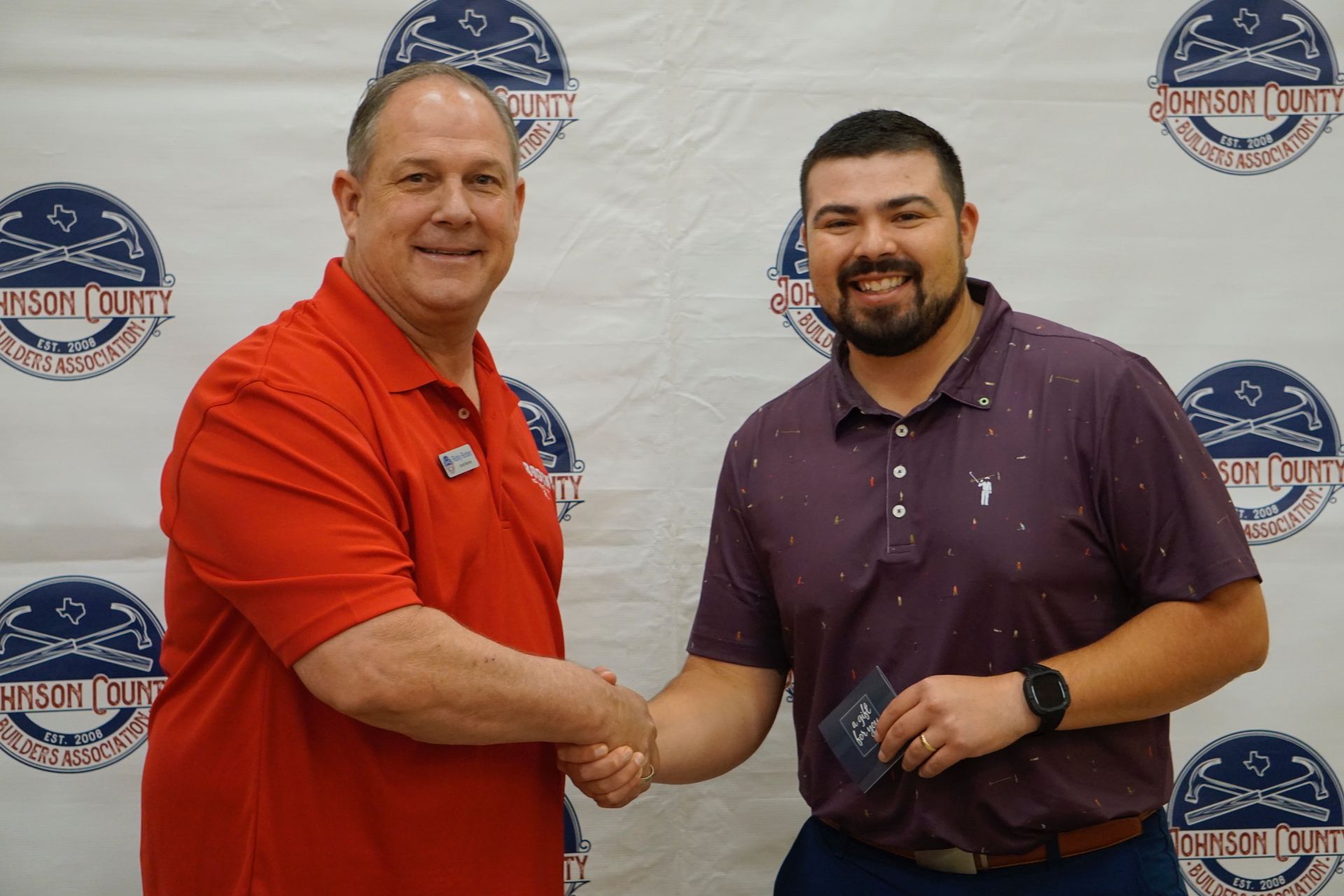 Two men are shaking hands in front of a wall with logos on it.