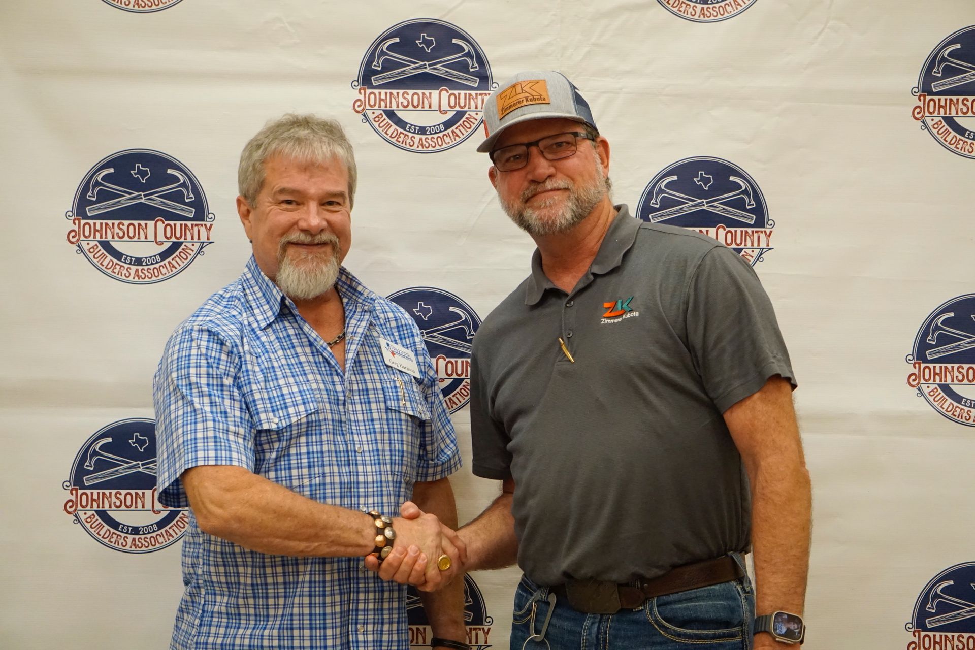 Two men are shaking hands in front of a wall with logos on it.