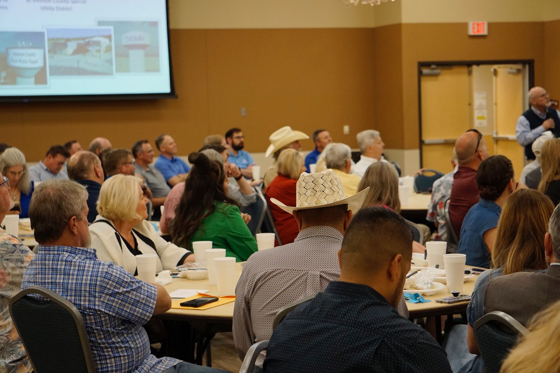 A group of people are sitting at tables in a room watching a presentation.