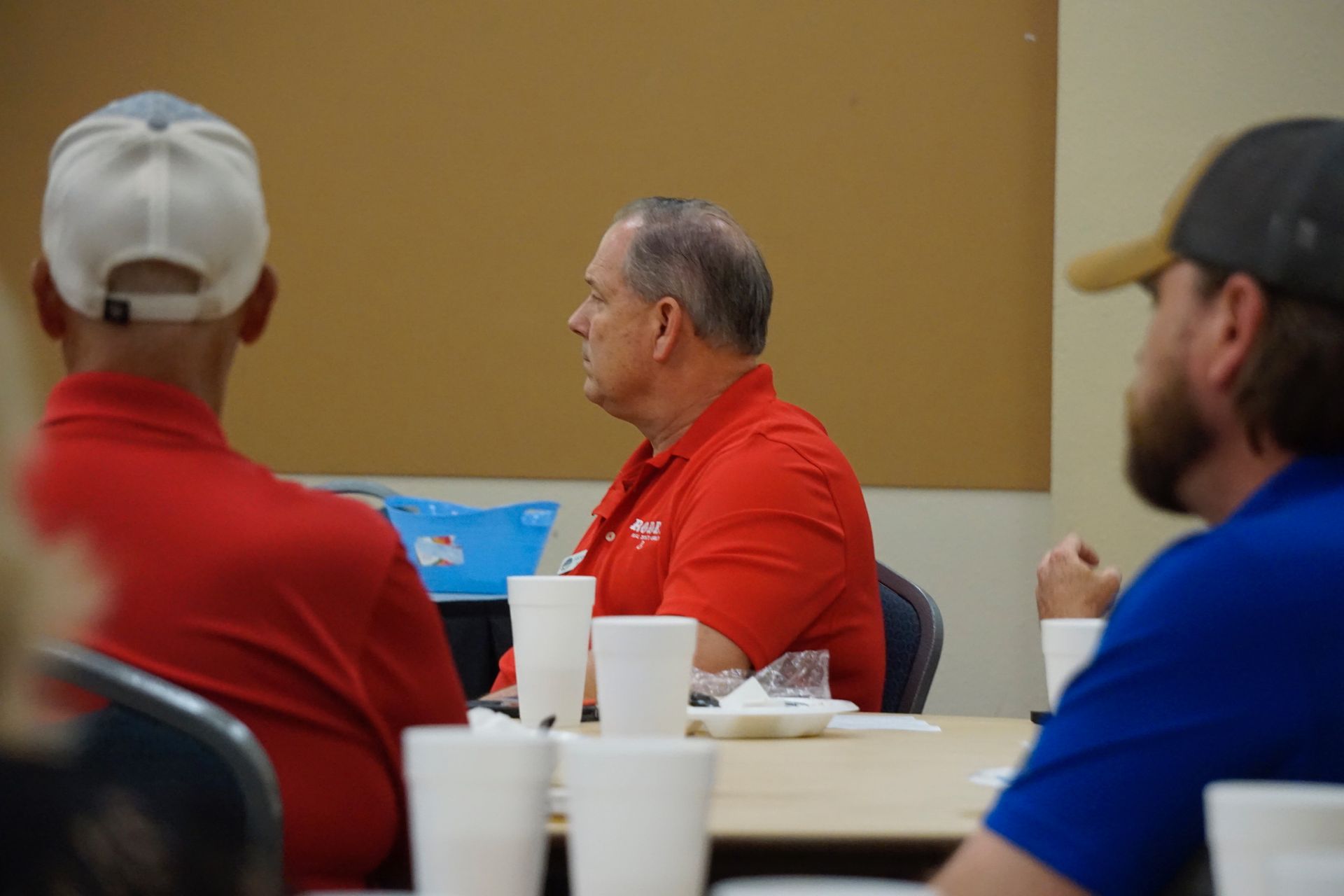 A man in a red shirt is sitting at a table with other men.