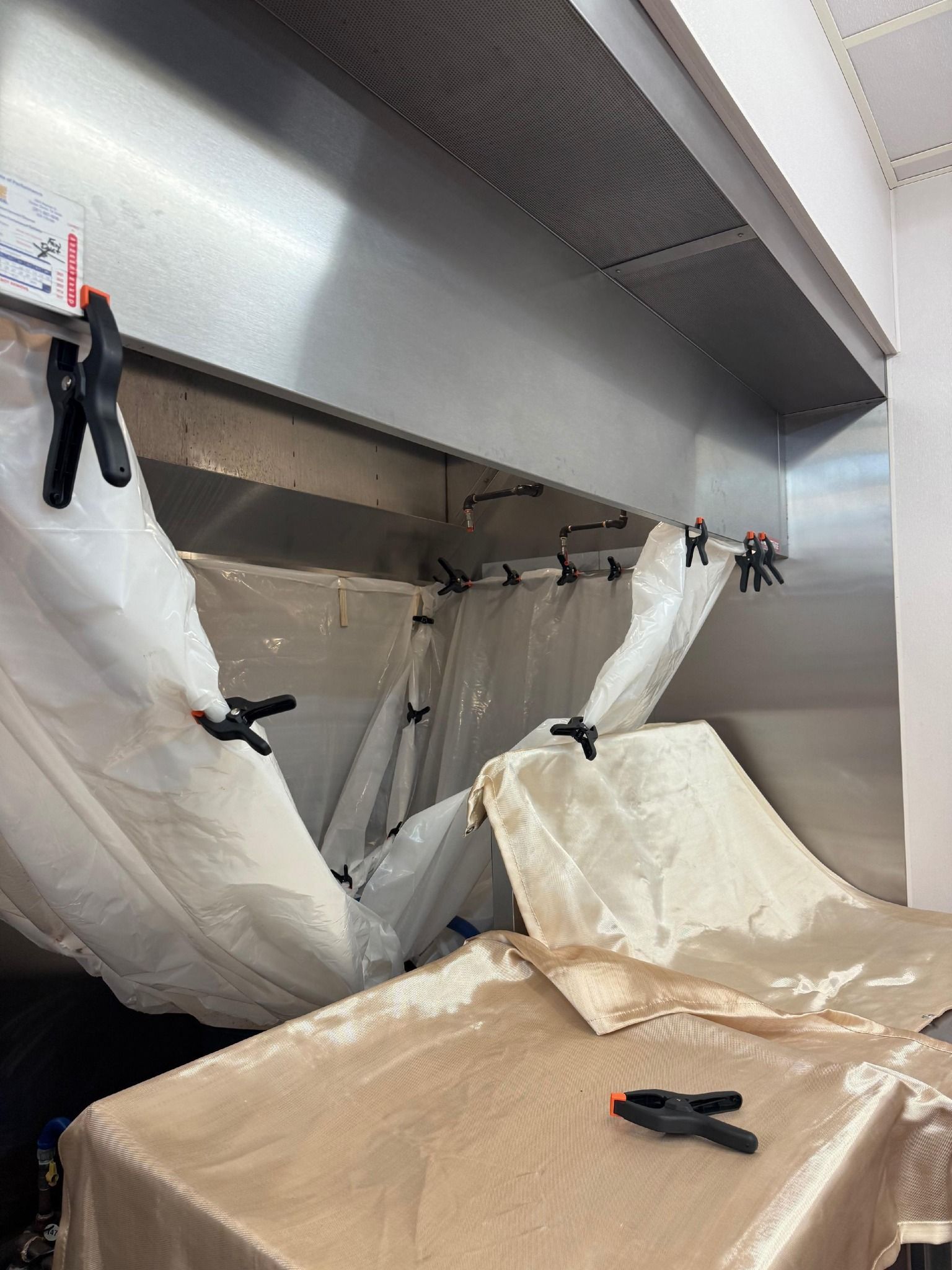 Stainless steel kitchen hood with a plastic structure held together by black clips.