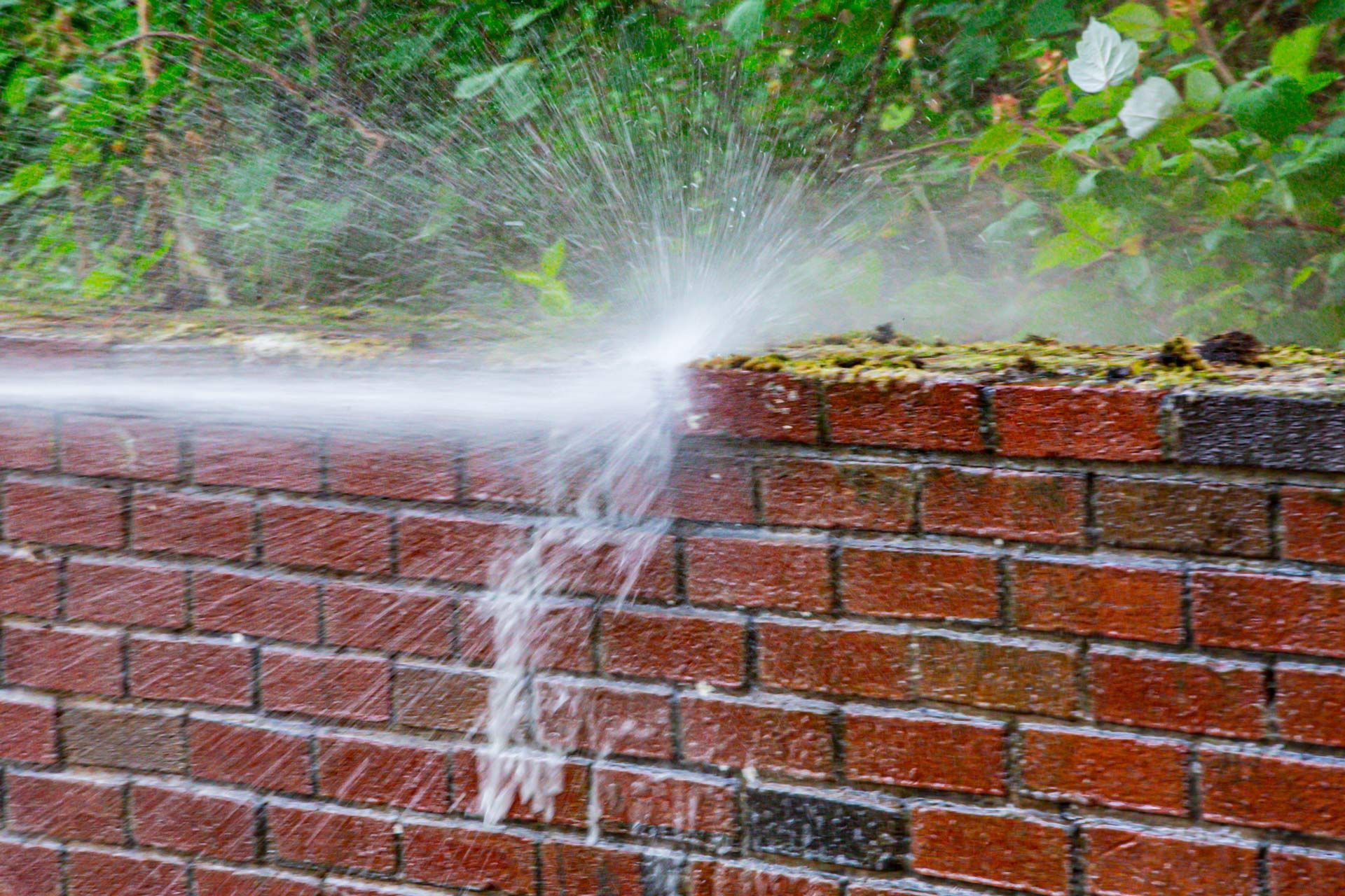 Water spraying from a damaged brick wall.