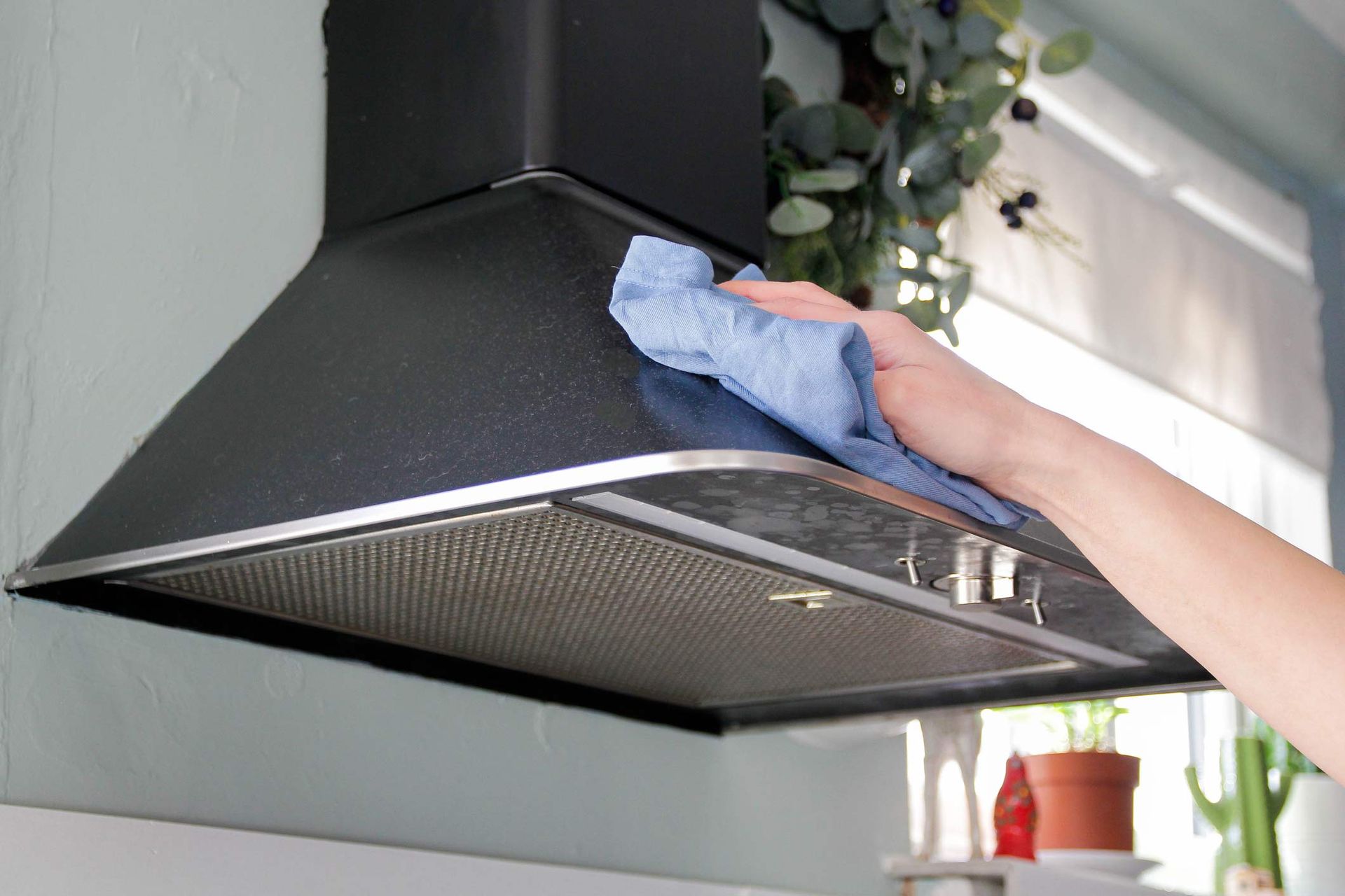 Person wiping down a black range hood with a blue cloth in a kitchen.
