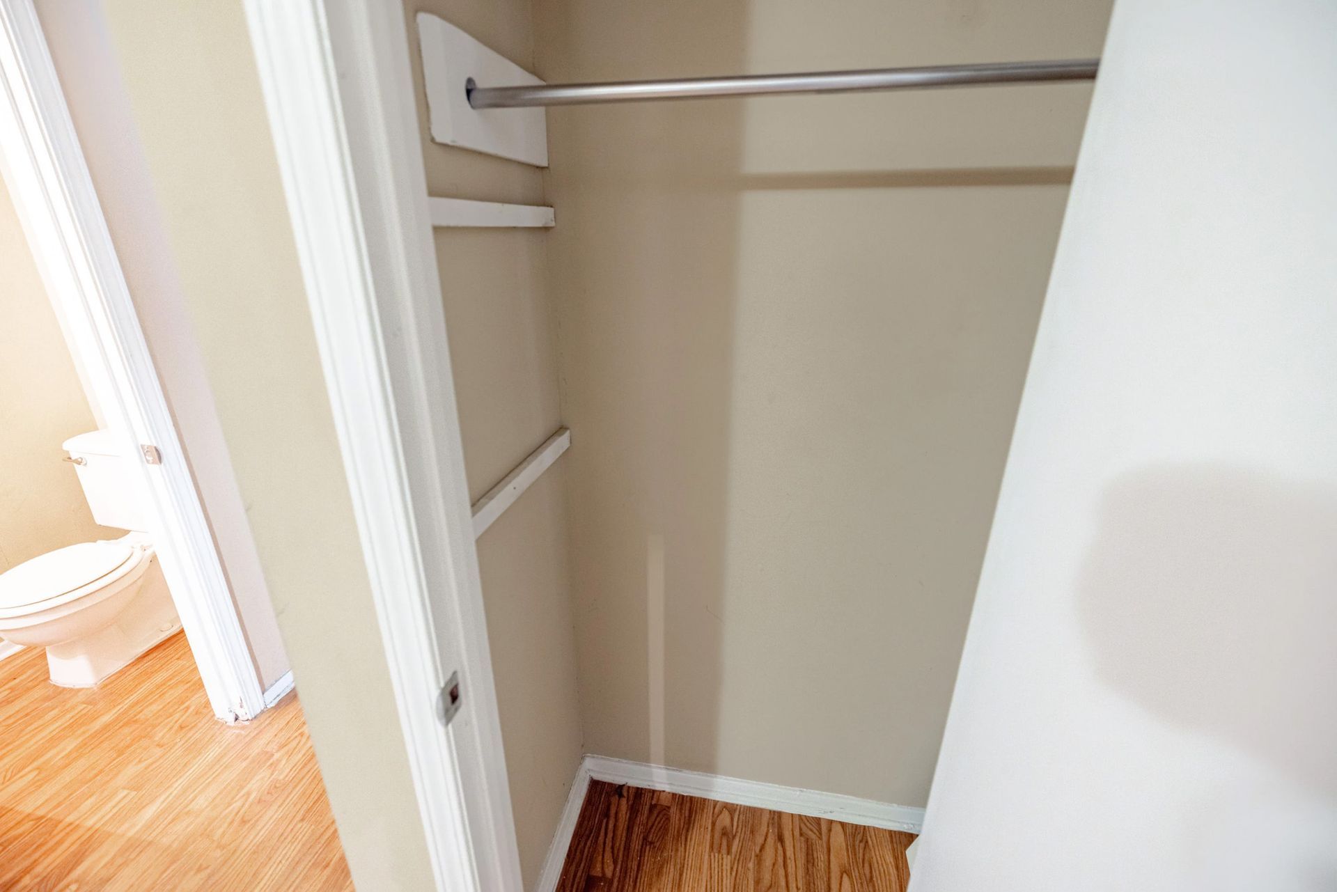 A closet in a house with a toilet and a wooden floor.