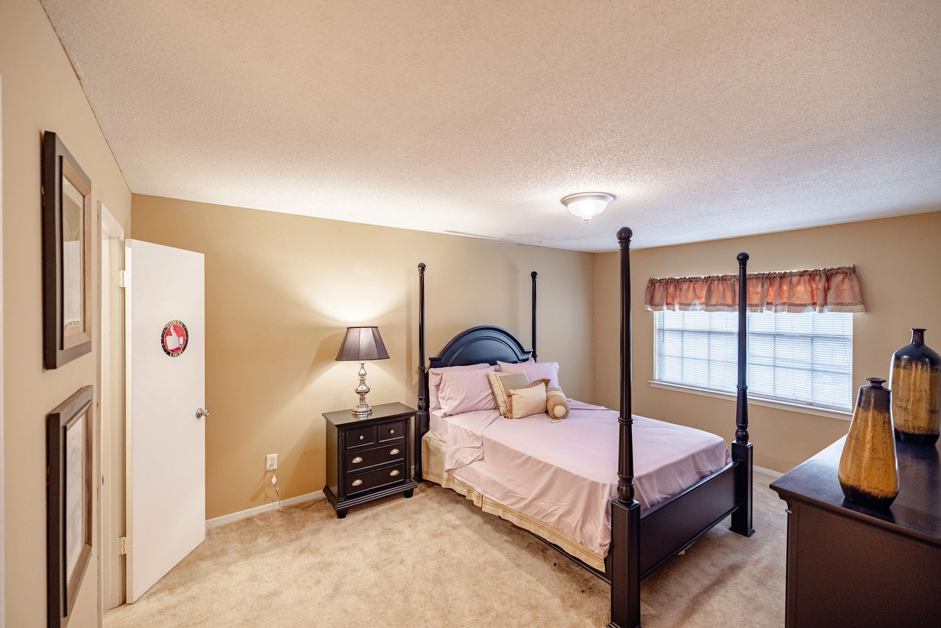 A bedroom with a four poster bed , nightstand , lamp and dresser.