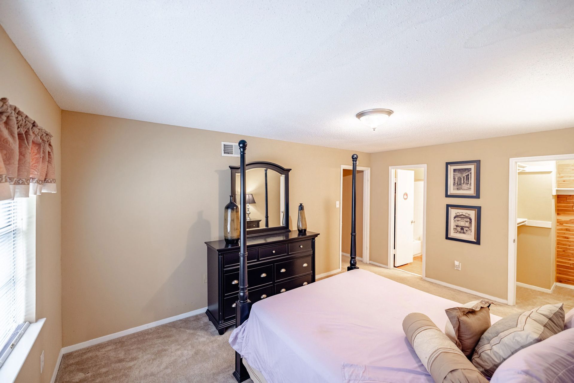 A bedroom with a four poster bed , dresser , mirror and window.