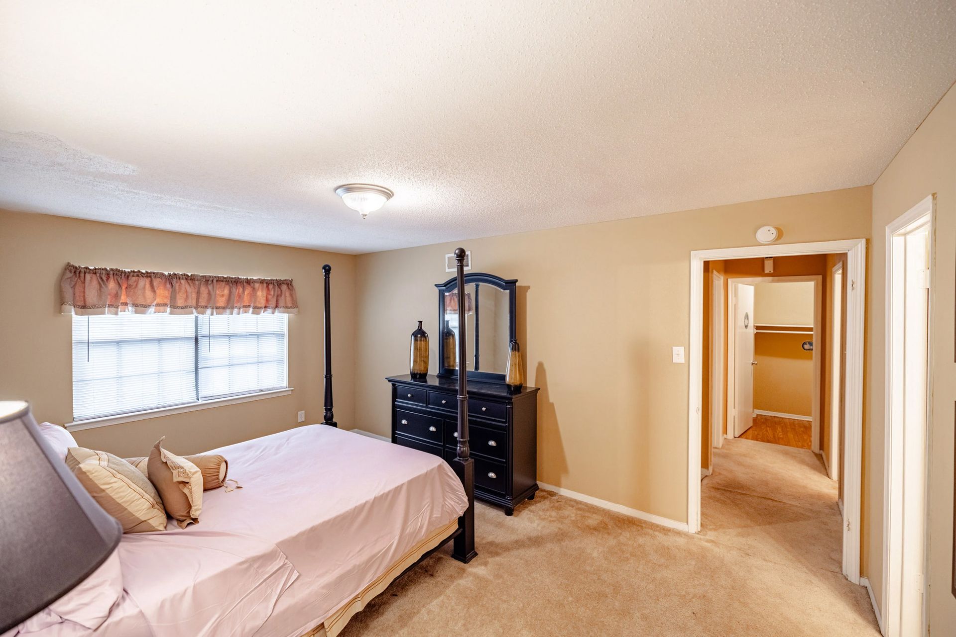 A bedroom with a bed , dresser , mirror and window.