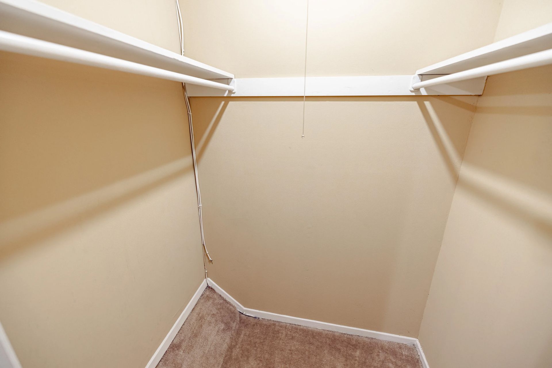 An empty walk in closet with a carpeted floor and white shelves.