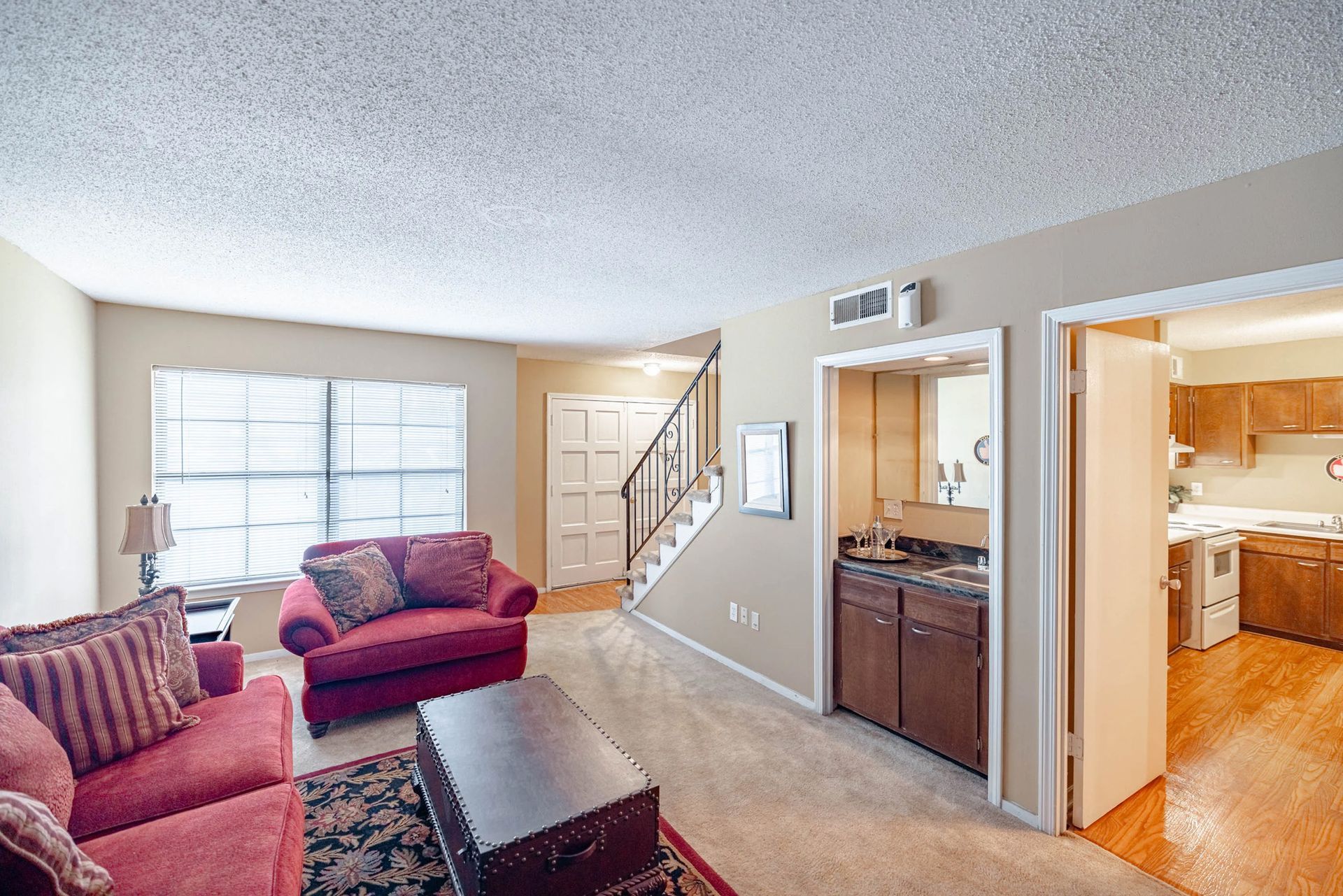 A living room with a couch , chair , coffee table and stairs leading to the kitchen.