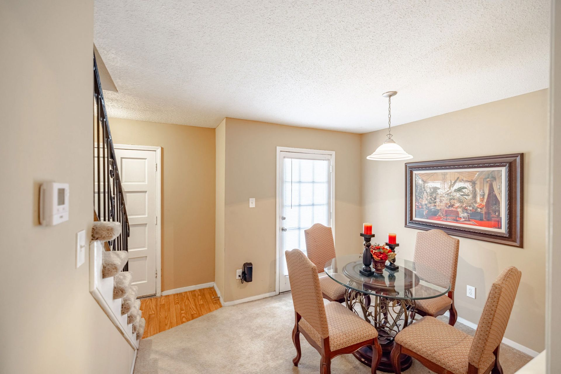 A dining room with a glass table and chairs and a picture on the wall.