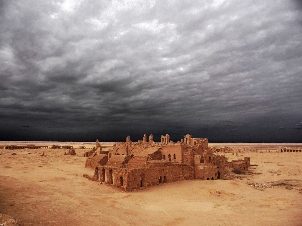 Eine Gruppe von Gebäuden inmitten einer Wüste unter einem bewölkten Himmel.