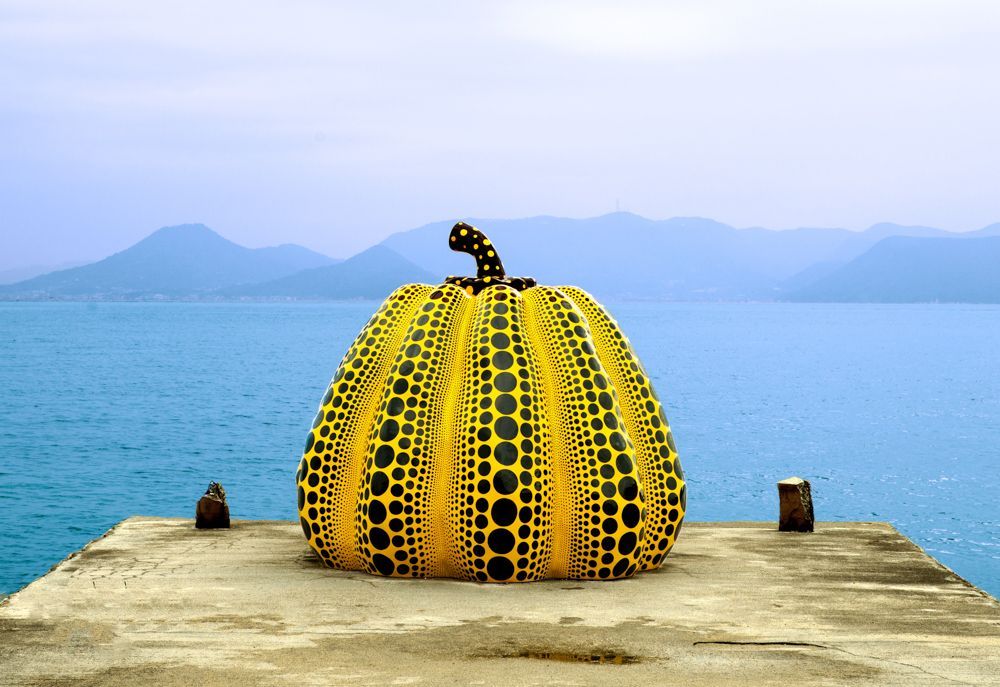 Ein grosser gelber Kürbis mit schwarzen Punkten liegt auf einem Steg in der Nähe des Meeres.