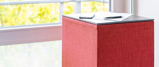 Auf einem Tisch neben einem Fenster steht eine rote Schachtel.