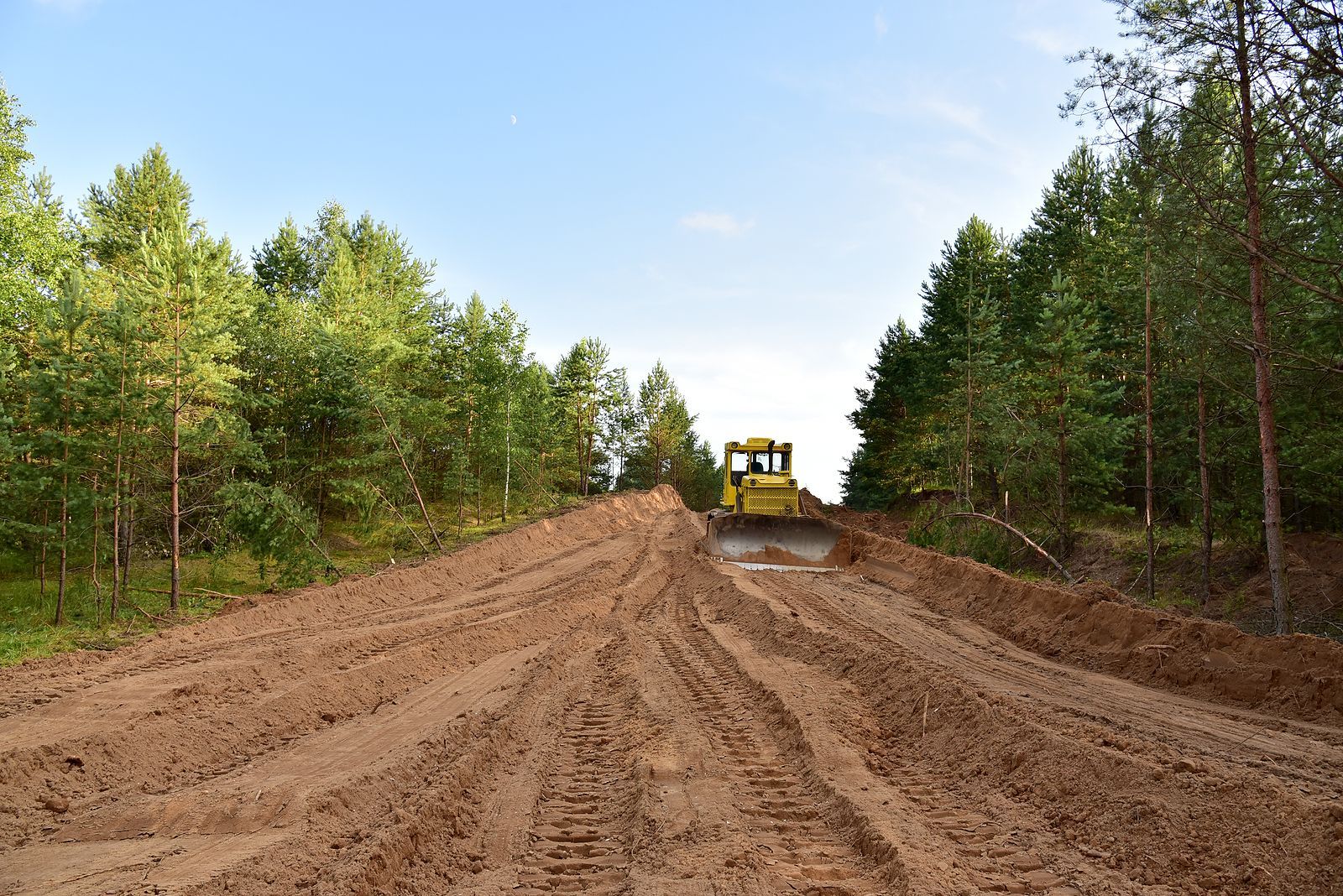 A bulldozer is driving down a dirt road in the woods.