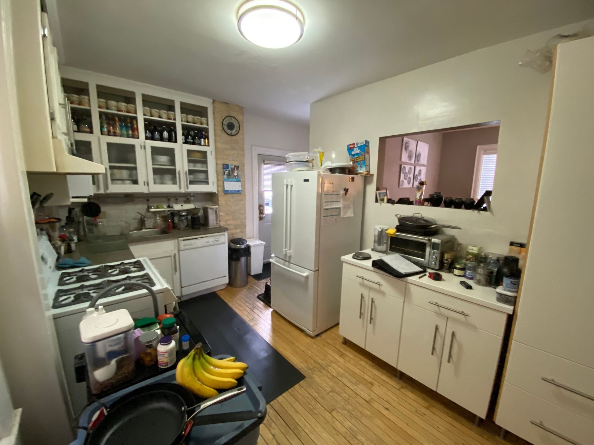 A kitchen with white cabinets , a stove , a refrigerator , a sink , and a trash can.