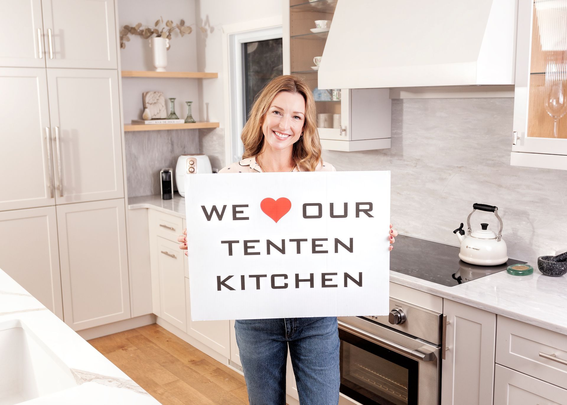 a woman is holding a sign in a kitchen that says `` we love our tenten kitchen '' .
