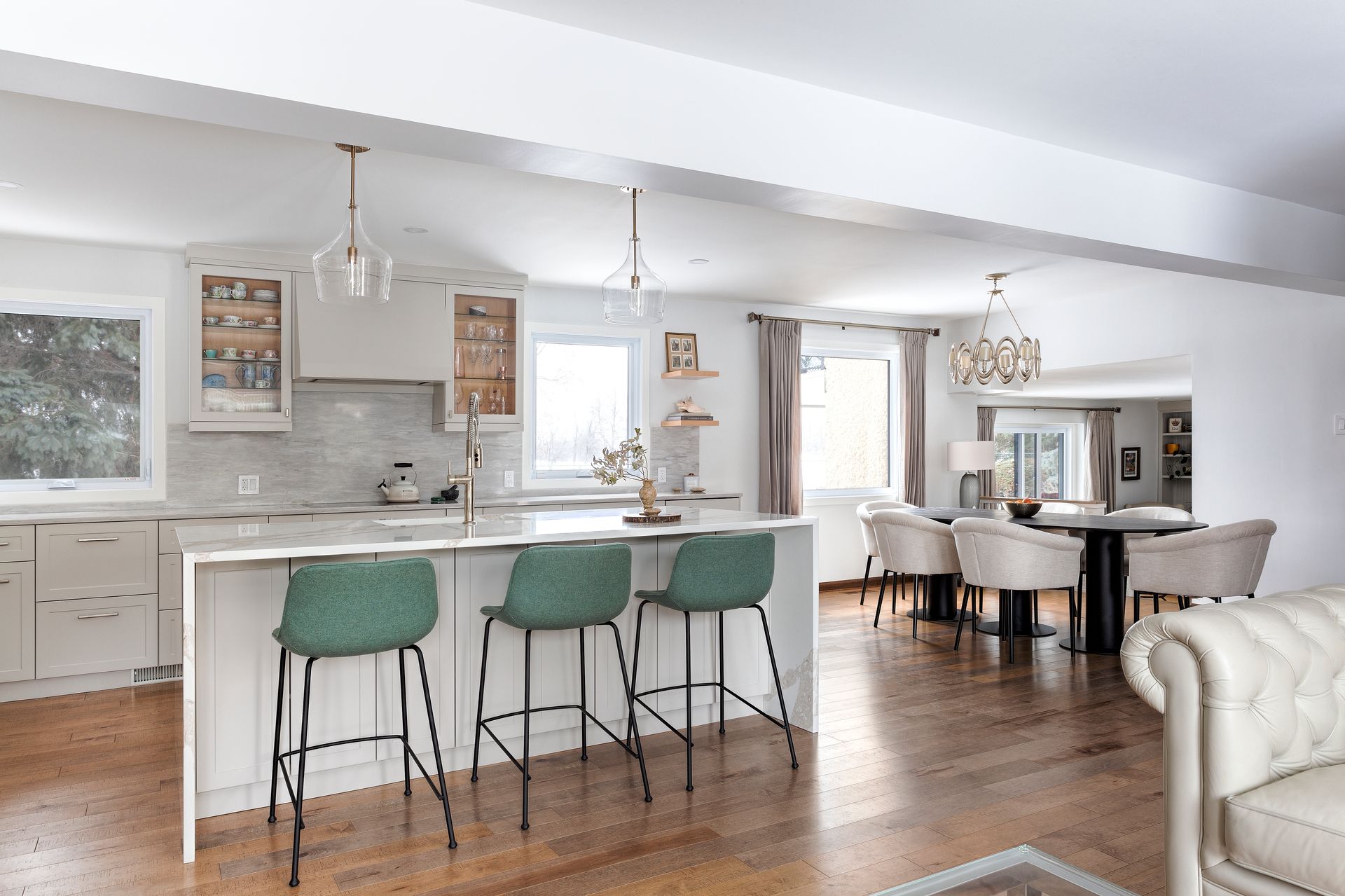a kitchen with white cabinets , green stools and a white couch .