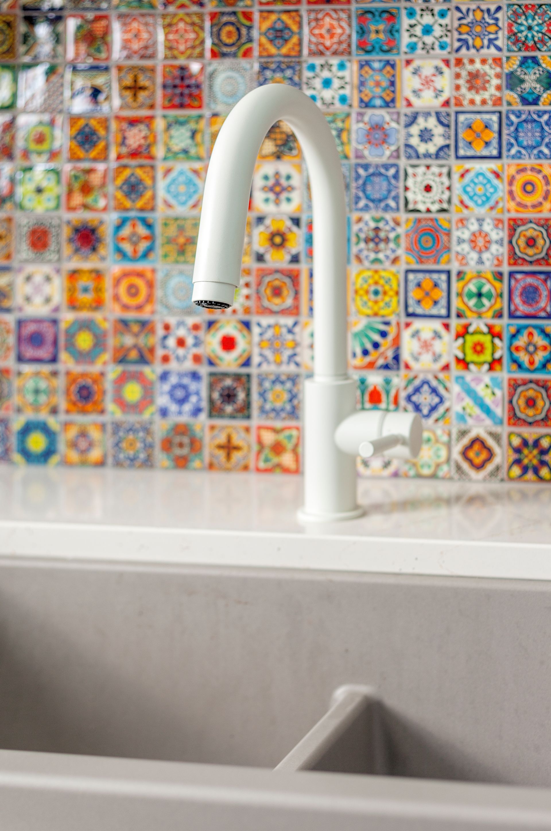 A kitchen sink with a white faucet and colorful tiles on the wall.