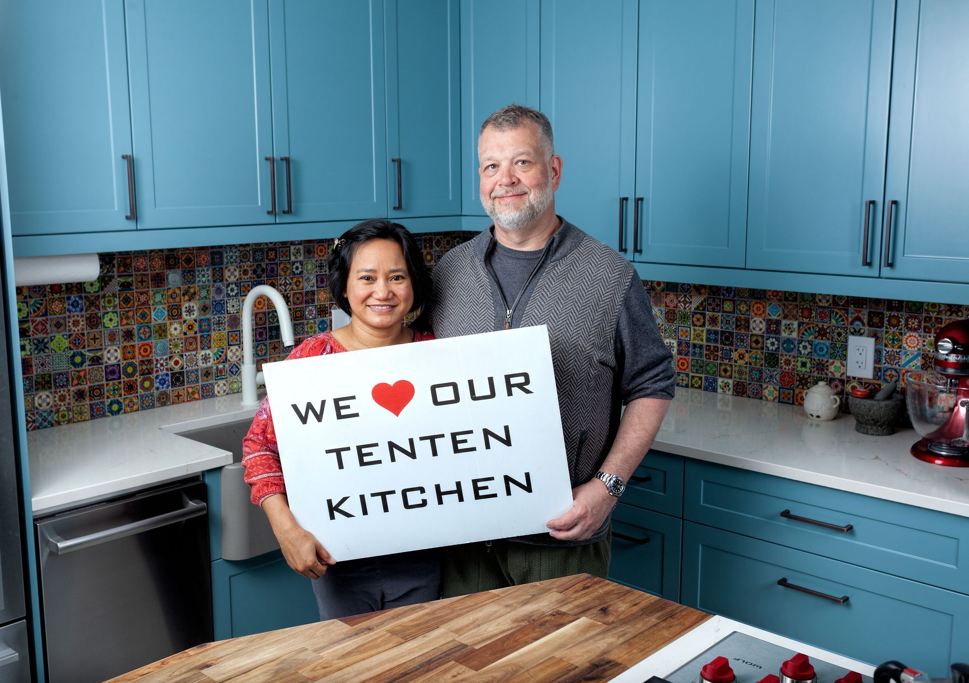 A man and a woman are holding a sign in a kitchen.