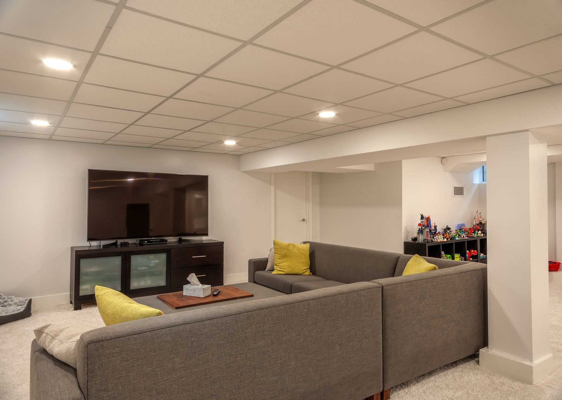 A living room in a basement with a couch and a flat screen tv.
