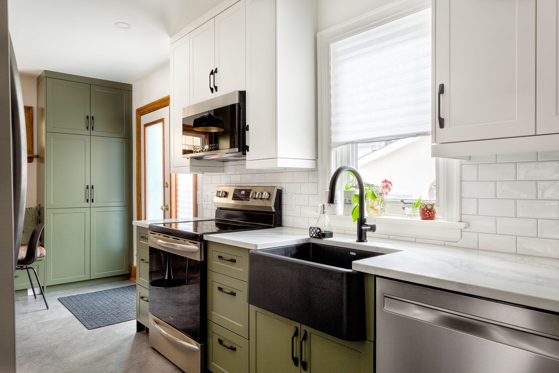 A kitchen with green cabinets , stainless steel appliances , a sink , and a window.